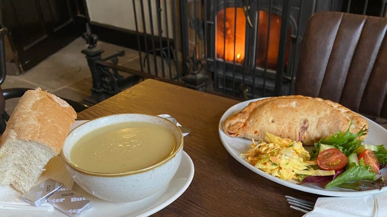 A bowl of soup and a pasty with salad garnish on a table in front of a fire at Grantham House.
